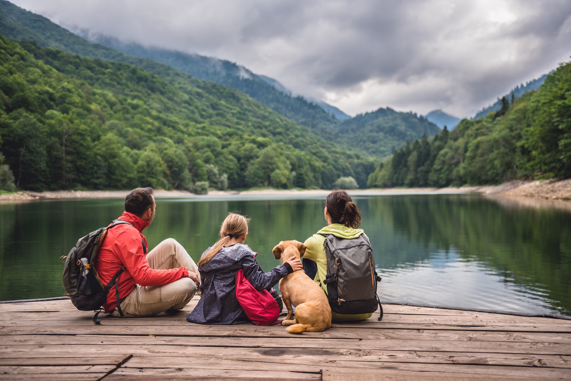 Family sitting on dock looking at lake with dog